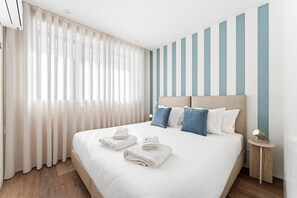 A neatly made bed with white and blue pillows, a wooden floor, and a striped wall. - GuestReady - Seaside retreat in Matosinhos (Matosinhos)