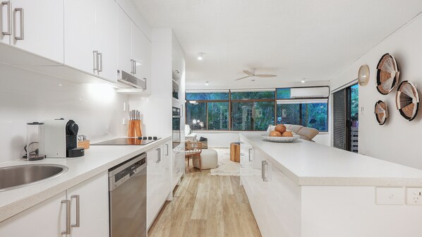 Una cocina moderna con armarios blancos, lavavajillas integrado y un amplio ventanal con vistas al exterior.