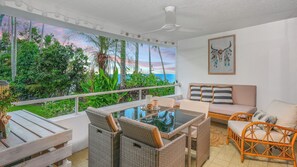 Ein Balkon mit Korbmöbeln, einem Glastisch und Blick auf das Meer.