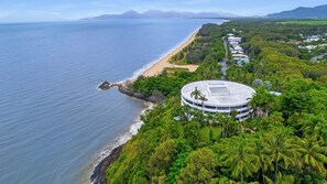 Ein Küstenhotel mit kreisförmigem Gebäude, direktem Zugang zum Strand und üppiger Bepflanzung.