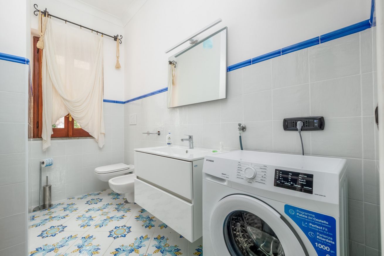 Un baño con lavadora, inodoro, lavamanos y espejo.