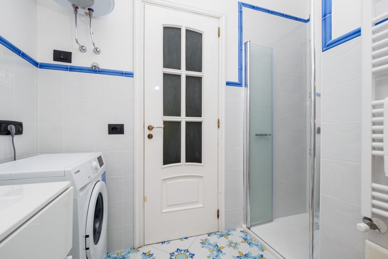 Un baño con lavadora, cabina de ducha de vidrio y suelo de baldosas con un diseño geométrico.