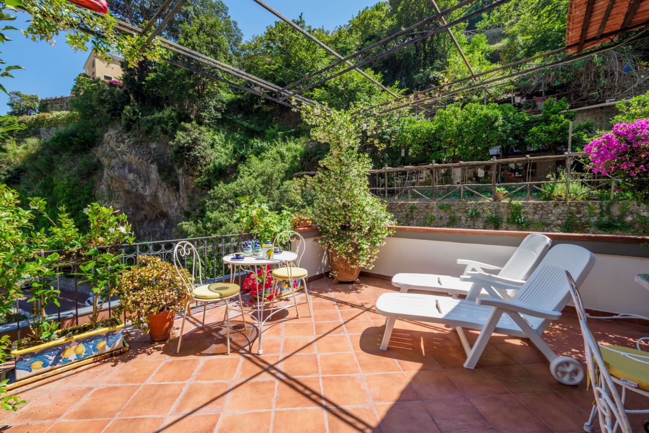 A terrace with a table and chairs, surrounded by potted plants and a view of a cliff.