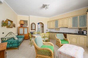 A compact living space with a sofa, dining table, wicker chairs, and a kitchen area with cabinets and a microwave. - Positano Elegant Terrace – Panoramic Home with Terrace in the Heart of Positano (Positano)