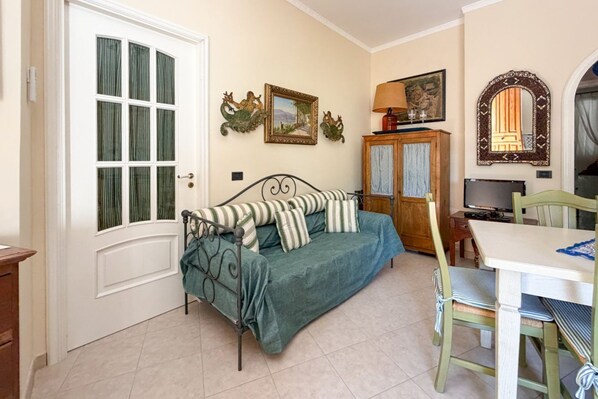 Een kamer met een groene bank, een houten kast, een tafel met stoelen en een deur voorzien van gordijnen.