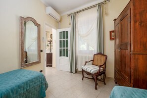 A room with two beds, a wooden wardrobe, a chair, and a door leading to another room. - Positano Elegant Terrace – Panoramic Home with Terrace in the Heart of Positano (Positano)