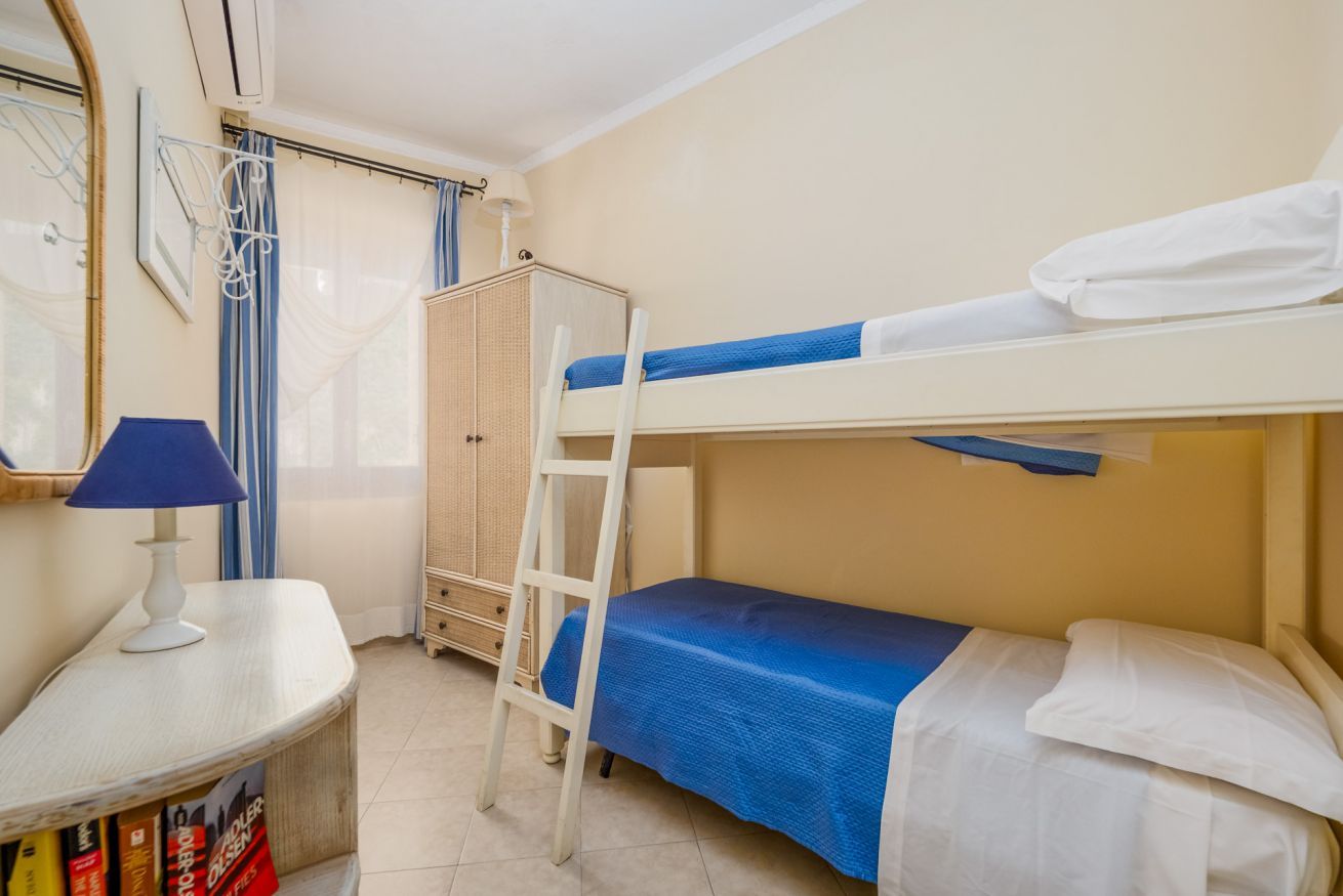 Een slaapkamer met stapelbed, bureau, lamp en garderobe.