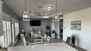 Una cucina moderna con isola in marmo, illuminazione a sospensione e zona pranzo con sedie bianche.