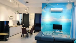 A modern living room with a large TV, a sofa, and a dining area with chairs and a table.