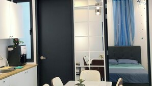 A modern hotel room with a dining area, a bed with blue curtains, and a black door.