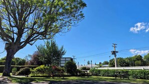 Una calle bordeada de árboles con mesas de picnic y una valla de piquetes blancos.