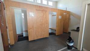 Baño público con separadores de madera, un bote de basura y una máquina de café.