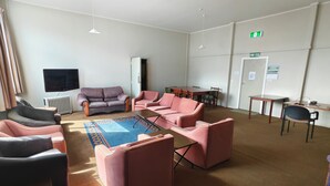 Una habitación con sofá, sillas, una mesa, televisor y señal de salida de incendios.