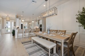A spacious dining area with a long wooden table, multiple chairs, a bench, and a hanging light fixture. - Edenfield Championship View Estate (Sumterville)