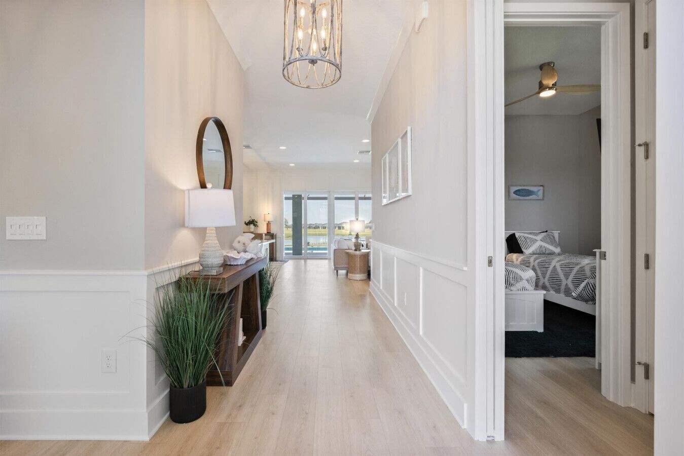 A hallway with a wooden floor, a mirror, a lamp, and a bed in the adjacent room. - Edenfield Championship View Estate (Sumterville)