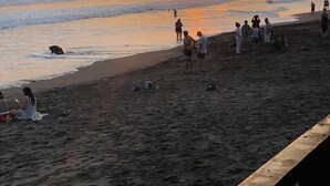 Una spiaggia con persone, un tramonto e onde.