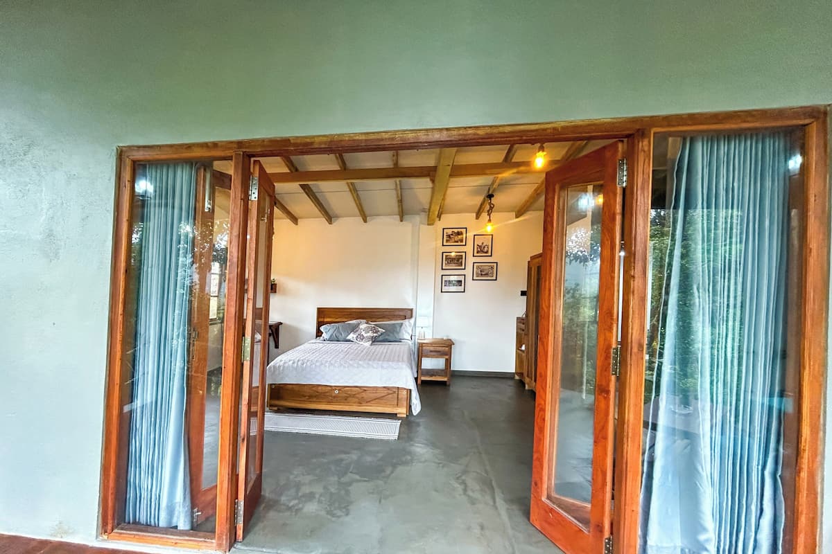 A bedroom with a bed, a nightstand, a dresser, and a window with curtains.