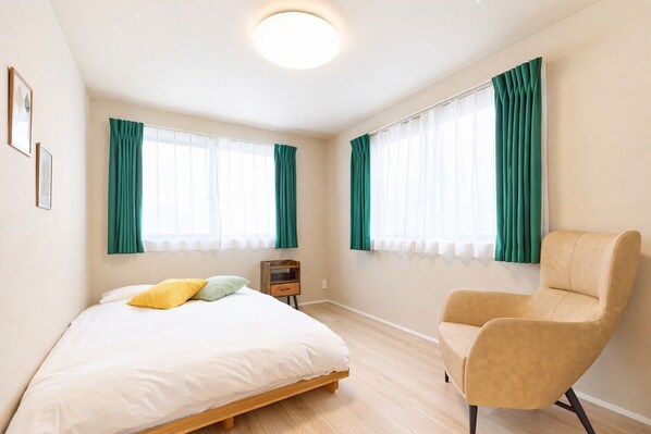 Ein Schlafzimmer mit einem Bett, einem Sessel, einem Nachttisch und zwei mit Vorhängen versehenen Fenstern.