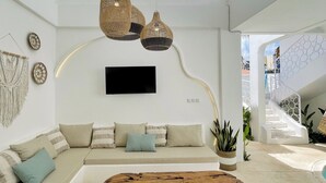 A modern living room with a sofa, a wooden coffee table, hanging wicker lamps, a TV mounted on the wall, and a staircase with a white railing. - Casa Nimare (Ungasan)