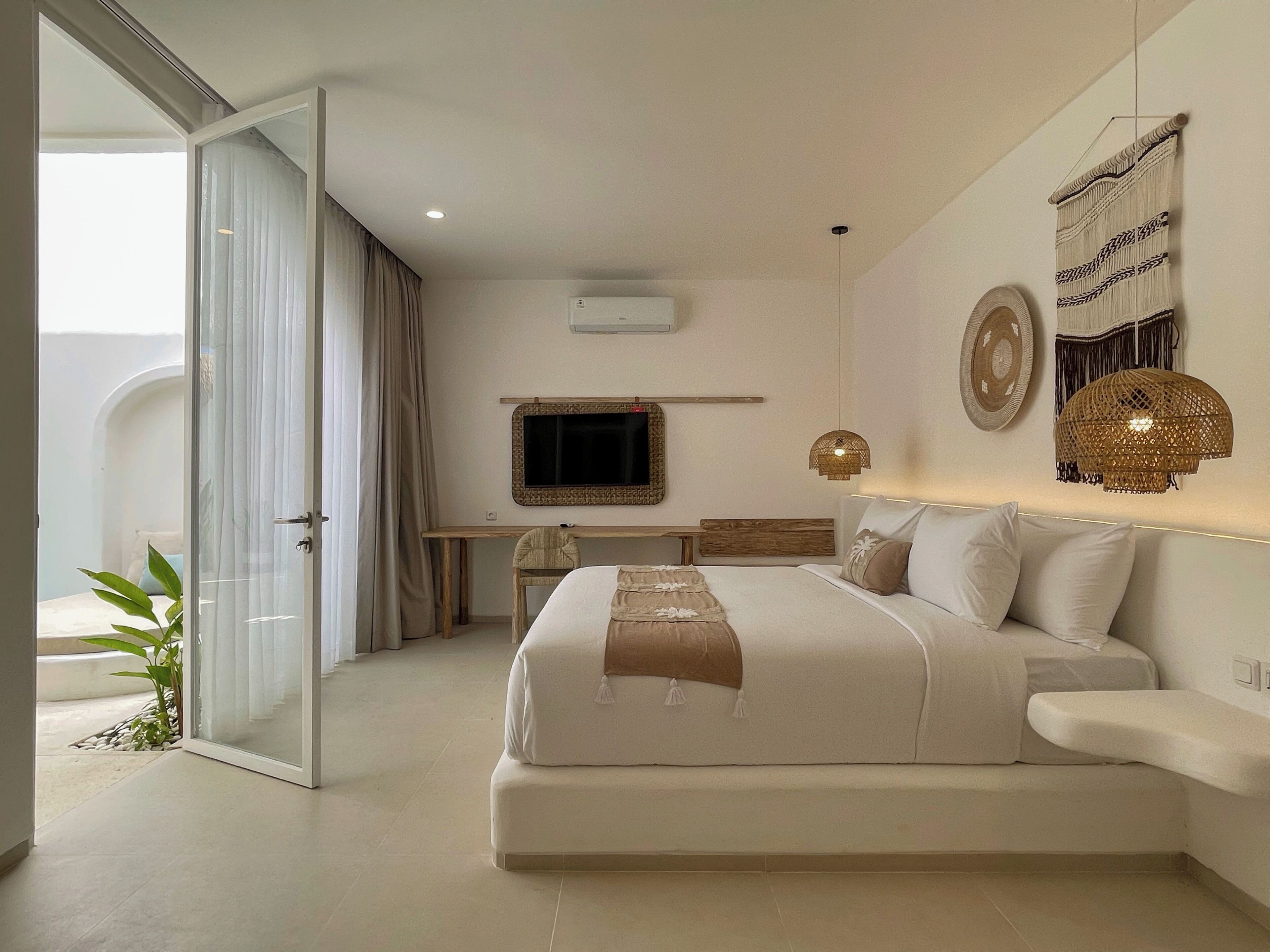 A modern bedroom with a large bed, a desk, a television, and a balcony with curtains.