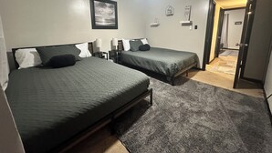 Een hotelkamer met twee bedden, een plafondventilator, een ingelijst kunstwerk aan de muur en een deur naar een andere kamer.
