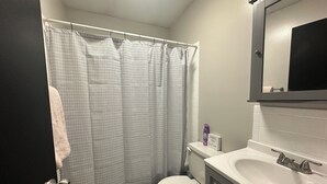 Een badkamer met douchegordijn, toilet, wastafel en spiegel.