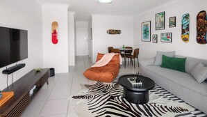 Una sala de estar moderna con un televisor de pantalla plana, un sofá, una mesa de centro y un comedor con sillas.