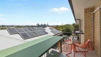 A balcony with solar panels, a table, chairs, and a view of a city skyline.