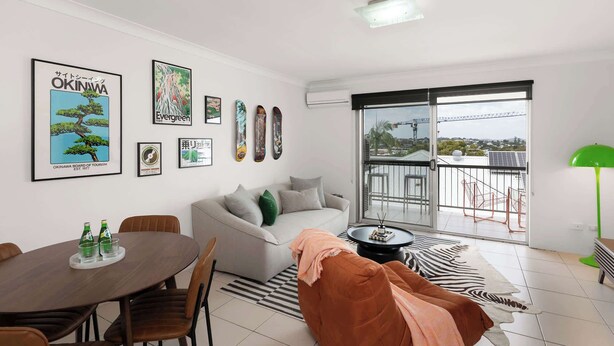 Una sala de estar moderna con un sofá, una mesa de comedor con sillas, un balcón con vistas y varias fotografías enmarcadas en la pared.