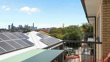 A balcony with a table and chairs, solar panels on the roof, and a city skyline in the background.