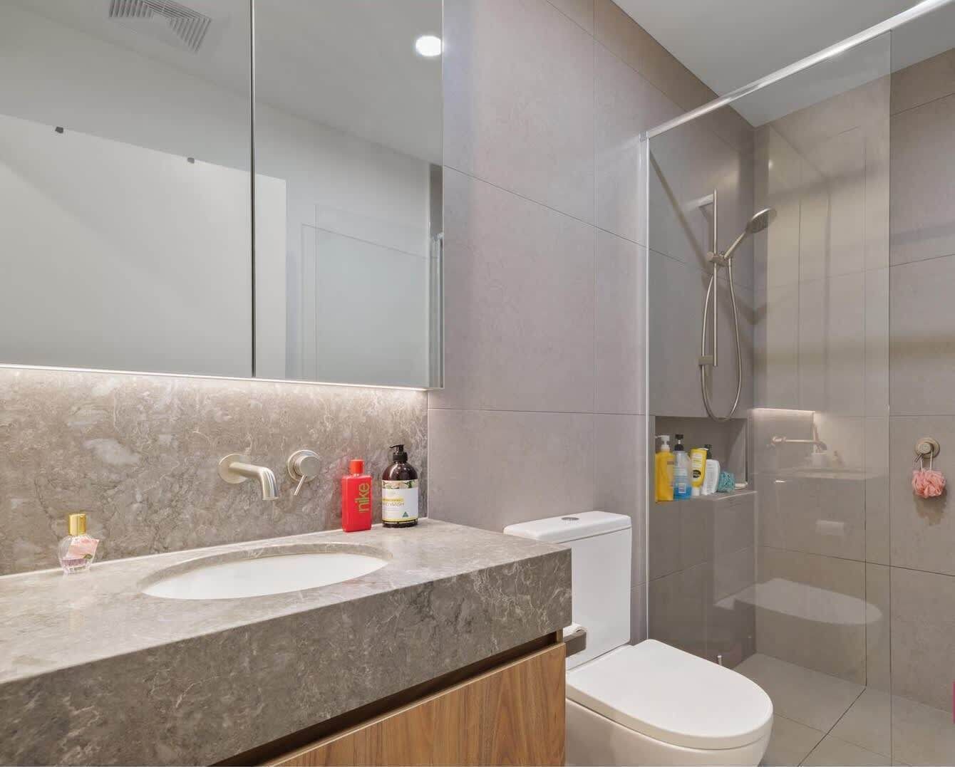 A modern bathroom with a marble sink, a glass shower enclosure, and a toilet.