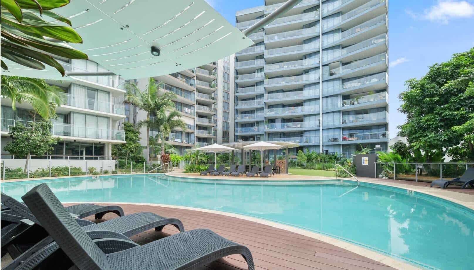 Un hôtel moderne doté d’une piscine, de chaises longues et d’un espace salon abrité.