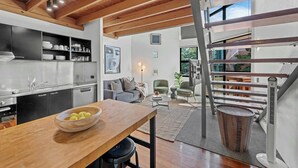 A modern kitchen with a wooden dining table, a sofa, and a staircase with a metal railing. - 3-Bed Teneriffe Apartment - Pool | Gym | Parking (Teneriffe)
