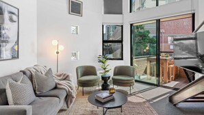 A modern living room with a grey sofa, two armchairs, a coffee table, and a large window with a view of a building. - 3-Bed Teneriffe Apartment - Pool | Gym | Parking (Teneriffe)