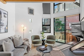 A modern living room with a grey sofa, two armchairs, a coffee table, and a large window with a view of a building. - 3-Bed Teneriffe Apartment - Pool | Gym | Parking (Teneriffe)