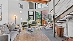 A modern living room with a staircase, large windows, and a view of the outside. - 3-Bed Teneriffe Apartment - Pool | Gym | Parking (Teneriffe)