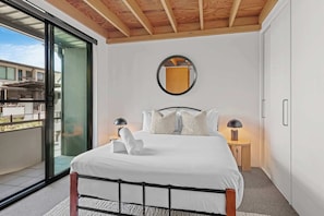 A bedroom with a bed, bedside lamps, a mirror, and a view through a glass door. - 3-Bed Teneriffe Apartment - Pool | Gym | Parking (Teneriffe)