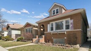 A two-story brick house with a front porch, a garage, and a well-maintained lawn. - Charming 5-bedroom Jefferson Park Bungalow near O’Hare (Chicago)