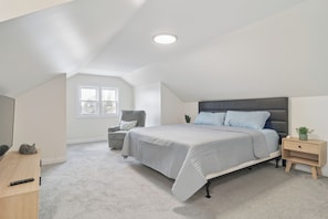 Ein Schlafzimmer mit Bett, Nachttisch, Stuhl, Schreibtisch und Fenster.