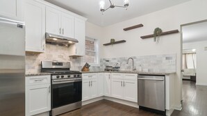 A modern kitchen with white cabinets, stainless steel appliances, and a wooden floor. - Charming 5-bedroom Jefferson Park Bungalow near O’Hare (Chicago)