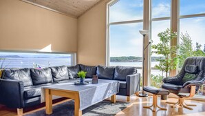 Un salon moderne avec un canapé en cuir, une table basse et un fauteuil, et une grande fenêtre donnant sur la mer.