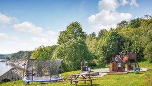 Une zone herbeuse avec un trampoline, une table de pique-nique et une petite structure en bois dotée d’un toboggan.