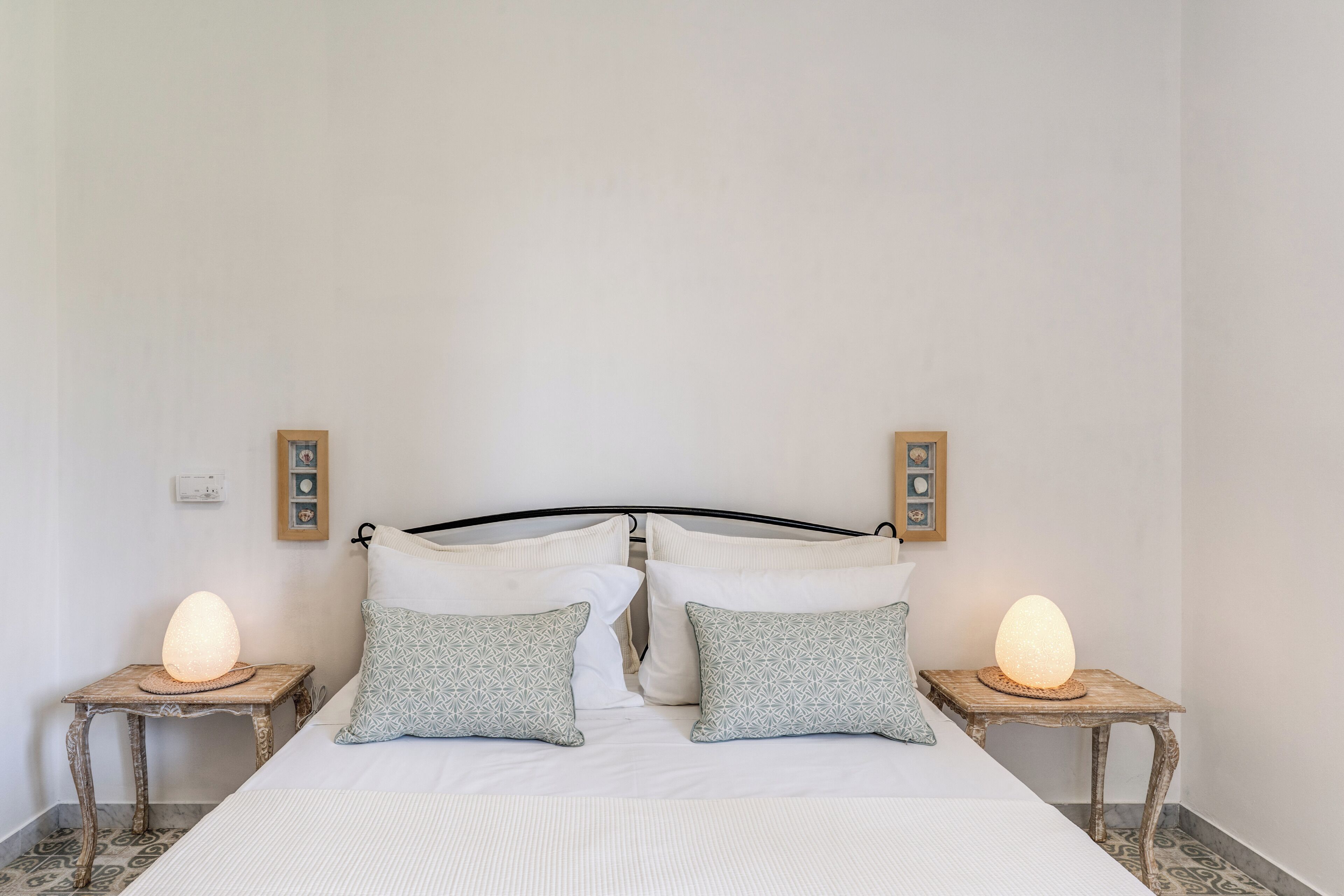 A bed with two pillows, a bedside table with a lamp, and a wall-mounted picture frame.