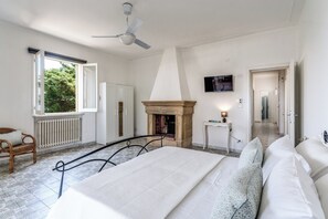 Un dormitorio con cama, chimenea, televisor y vistas al exterior.