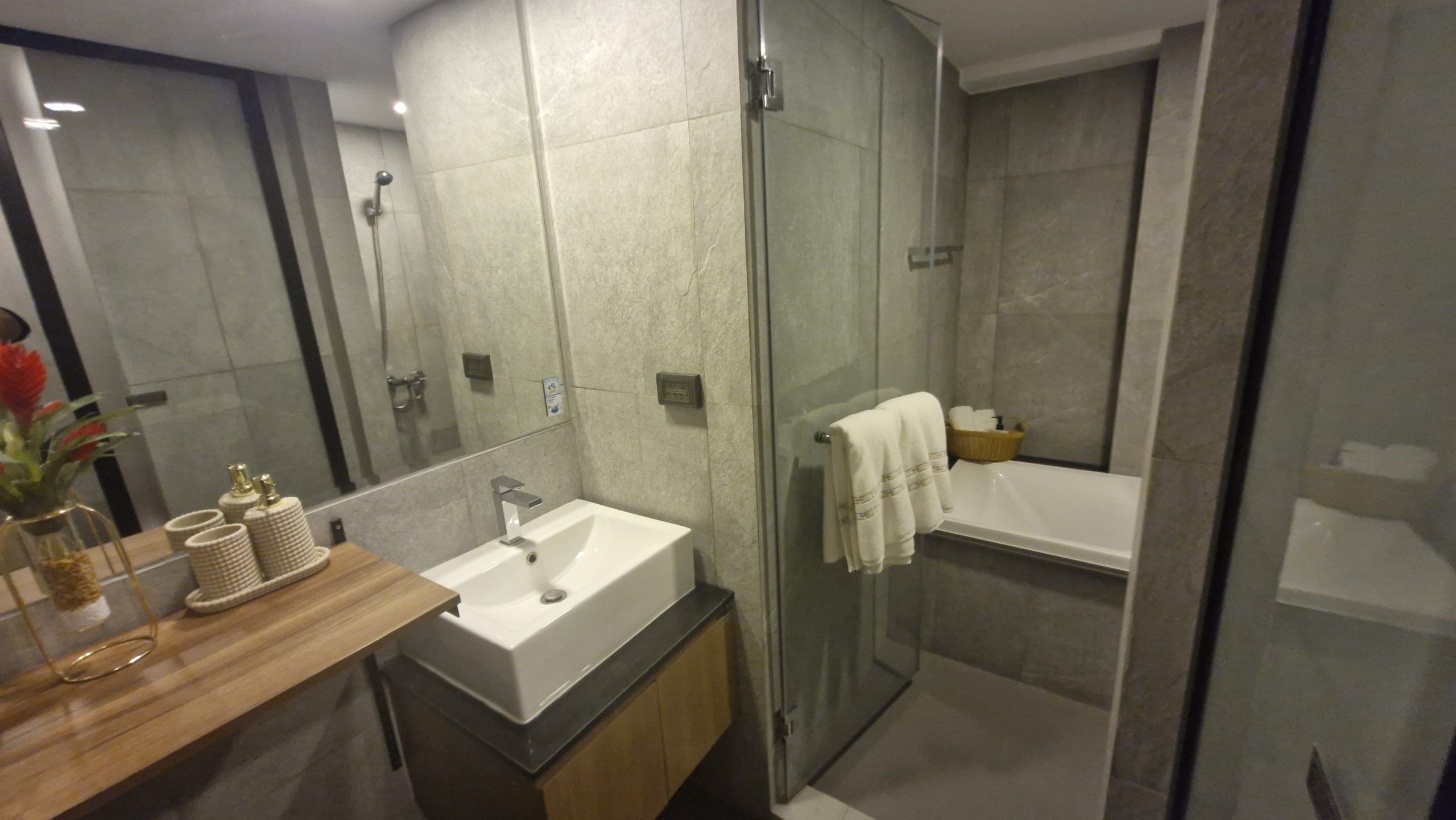 A modern bathroom with a glass-enclosed shower, a sink with a mirror, and a wooden vanity.