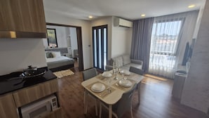 A modern hotel room with a dining area, a bed, a kitchenette, and a balcony with a view. - Triple J Suite (Si Racha)