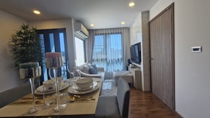 A modern living room with a dining area, a TV, and a large window. - Triple J Suite (Si Racha)