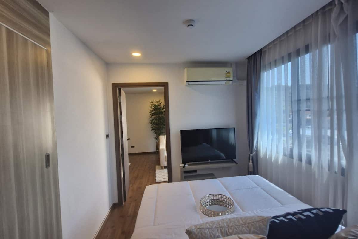 A hotel room with a bed, a TV, a window with curtains, and an air conditioning unit.