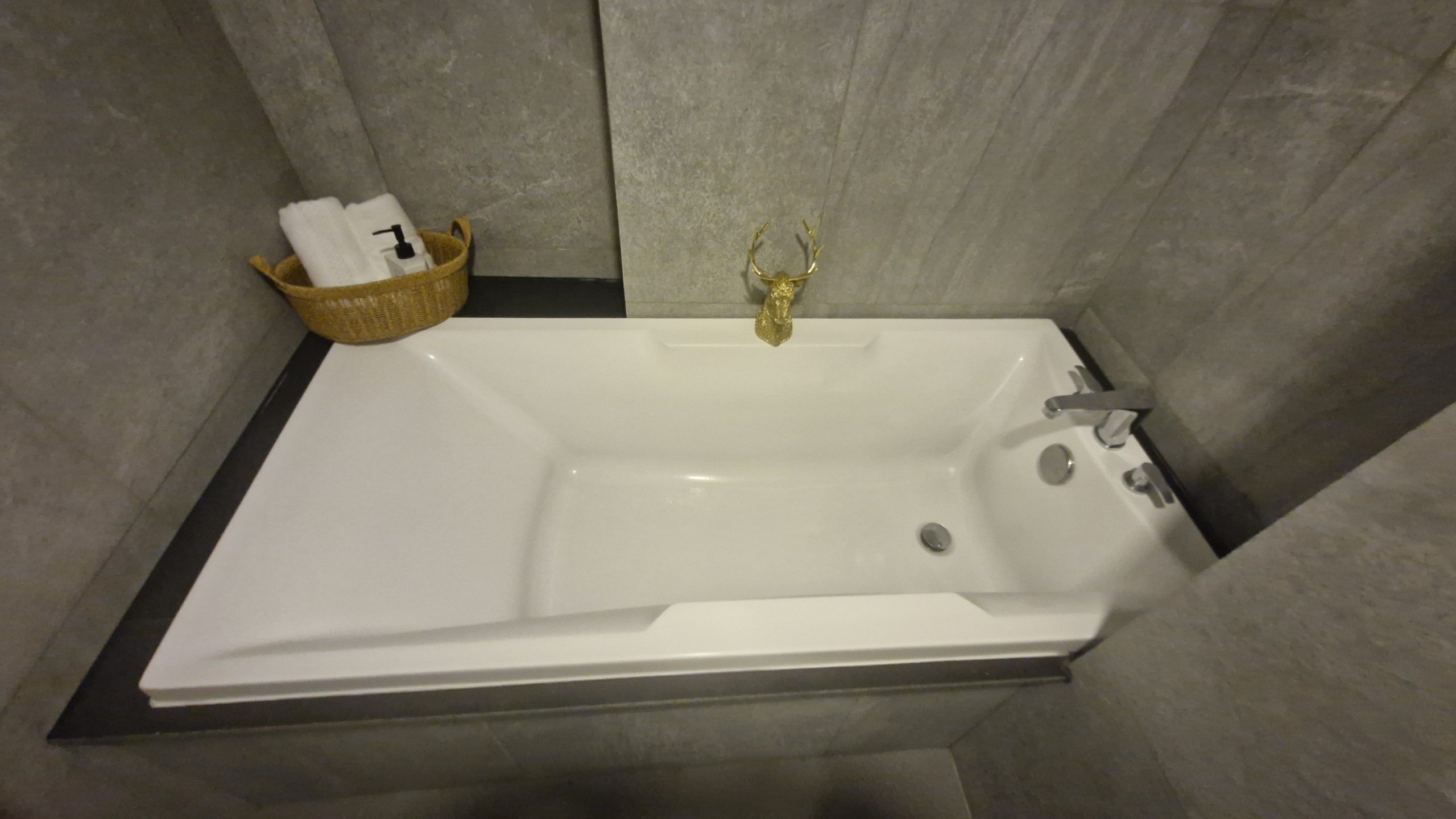 Uma banheira com uma torneira dourada, um cesto com uma toalha branca e um dispensador de sabonete fixado na parede.