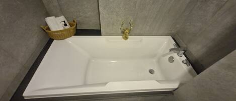 A bathtub with a golden faucet, a basket with a white towel, and a wall-mounted soap dispenser.